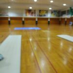Blurry indoor gymnasium with wooden floor, gymnastics mats along the floor, and colorful posters on the far wall.